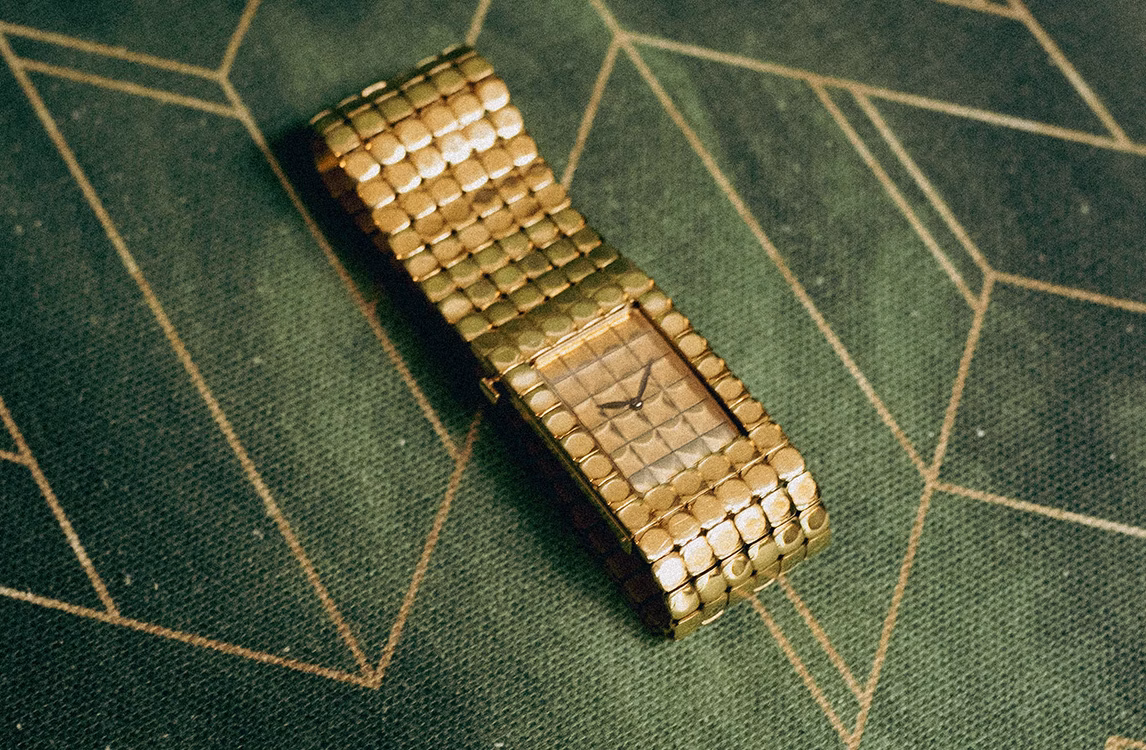 Audemars Piguet Cobra watch: a gold rectangular watch with a textured mesh bracelet laid on a green geometric fabric.
