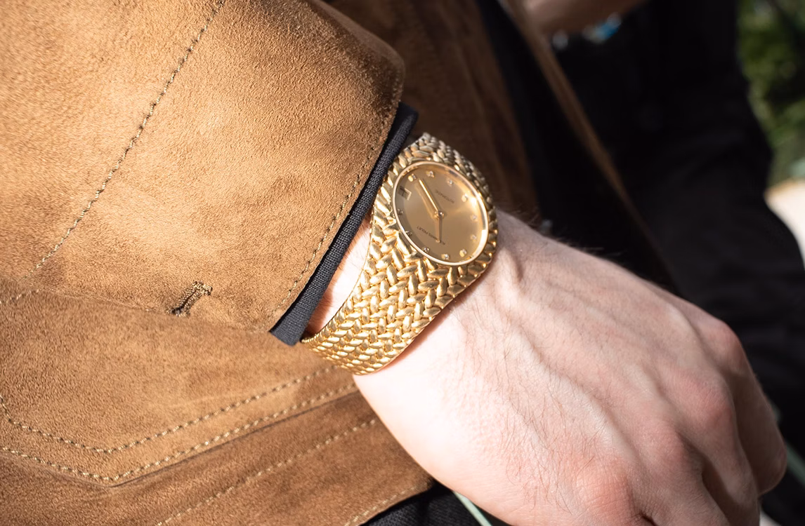 Audemars Piguet Cobra watch: close-up of a gold woven bracelet watch on a wrist, sleeve of a brown suede jacket.
