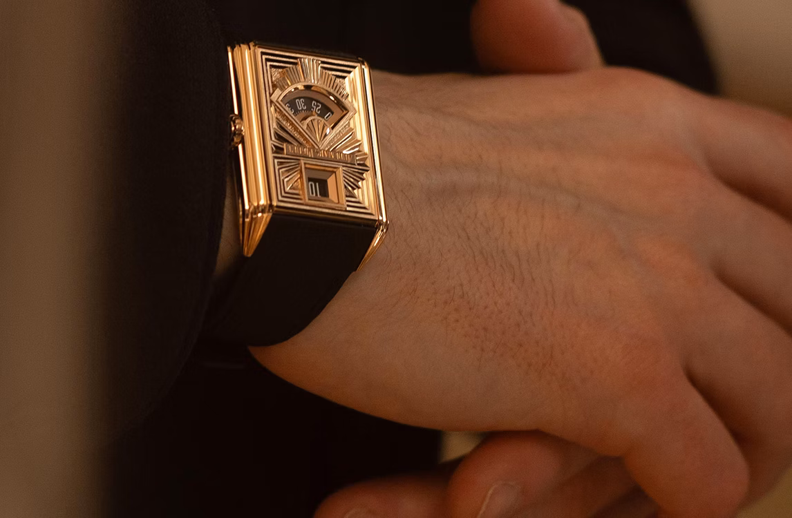 Close-up of a rose gold rectangular Art Deco watch with a retrograde display on a wrist.
