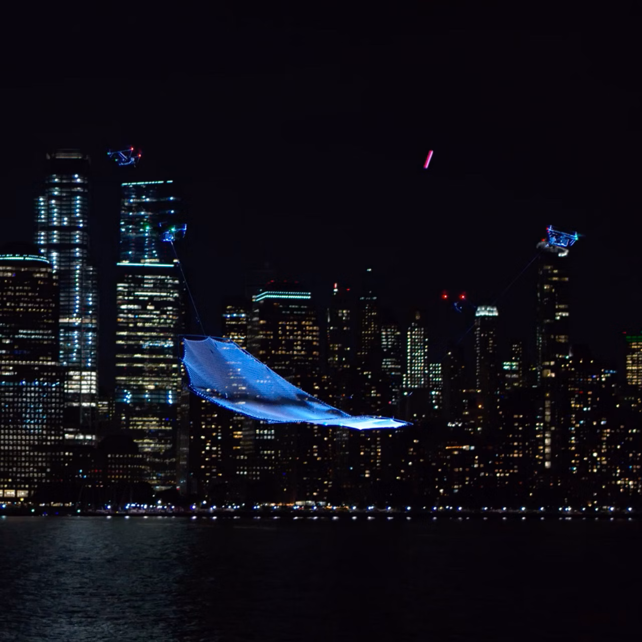 Vista de una ciudad de noche, con una red sostenida en el cielo por tres drones.