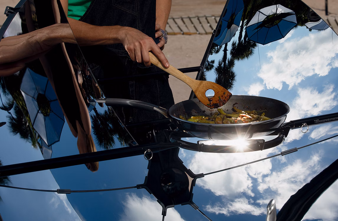 Una persona che cucina un piatto all'aperto su pannelli riflettenti come parte di Albedo di Thomás Saraceno