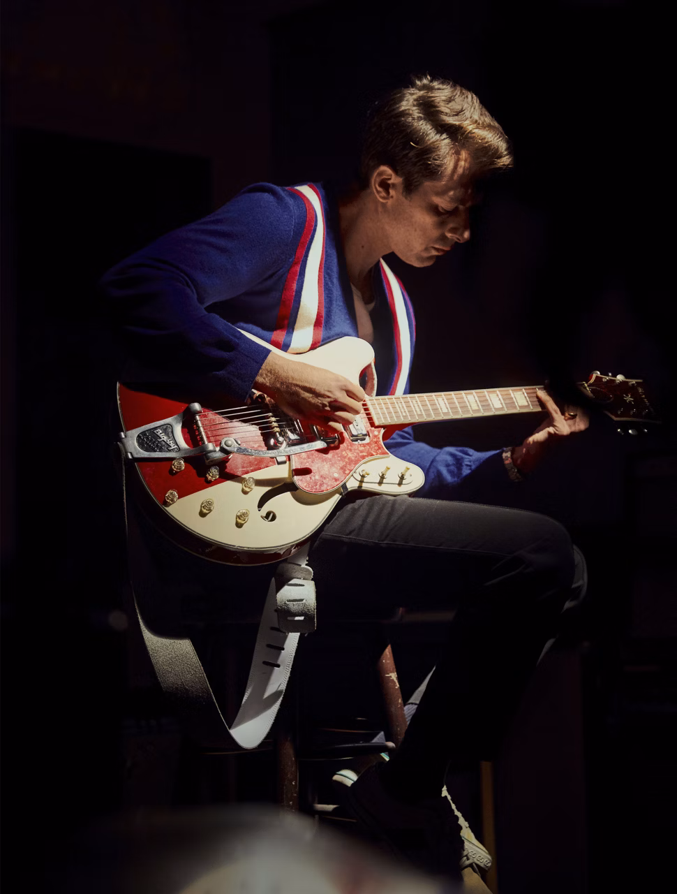 Mark Ronson seduto che suona la chitarra