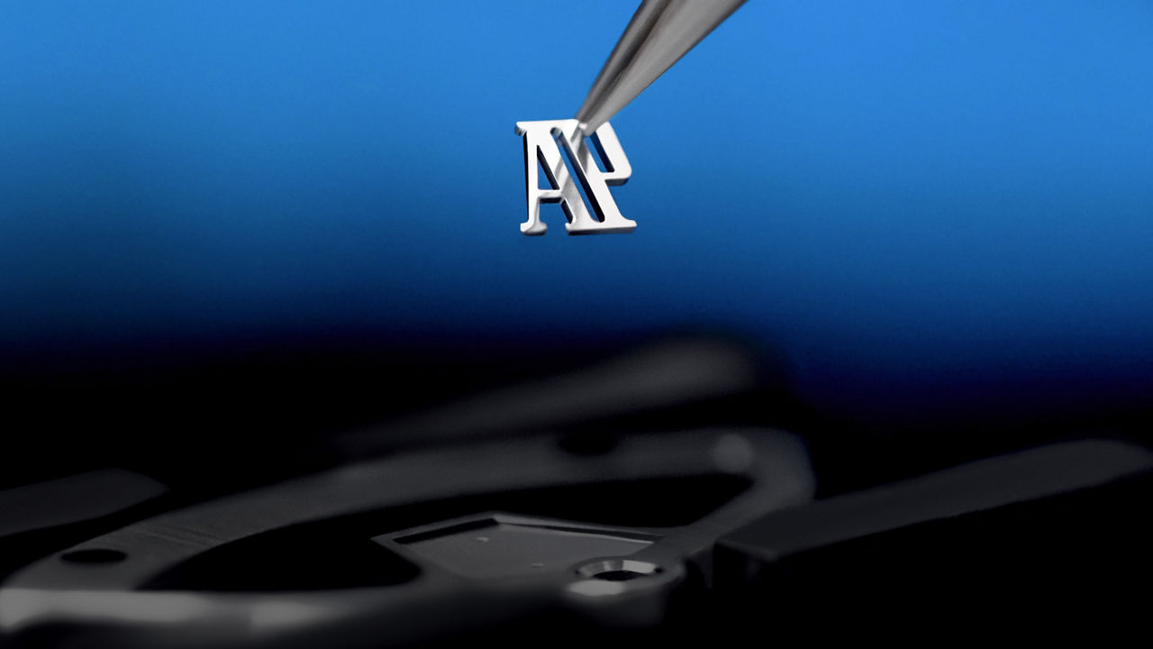 Close-up of an AP monogram delicately held by tweezers and about to be placed on a timepiece.