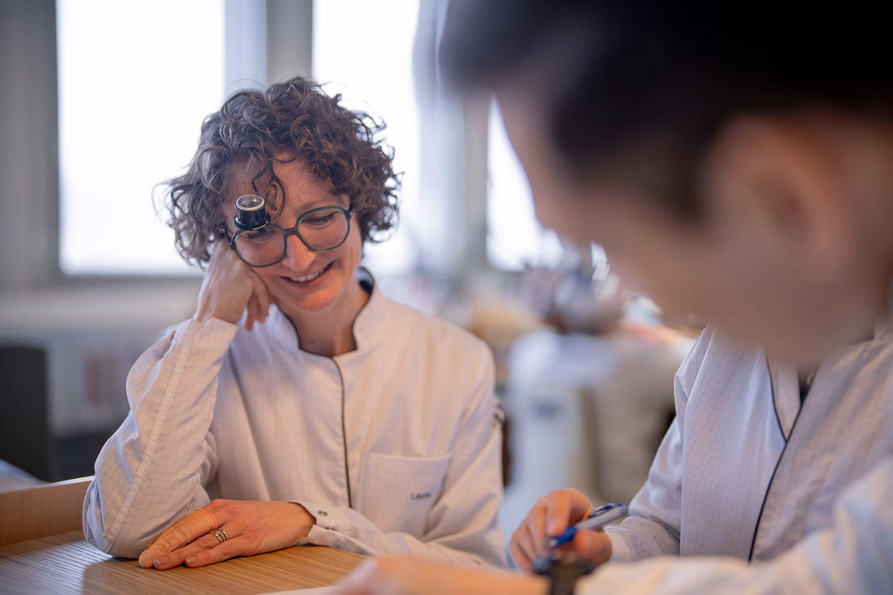 Female watchmaker having a friendly conversation with another watchmaker.