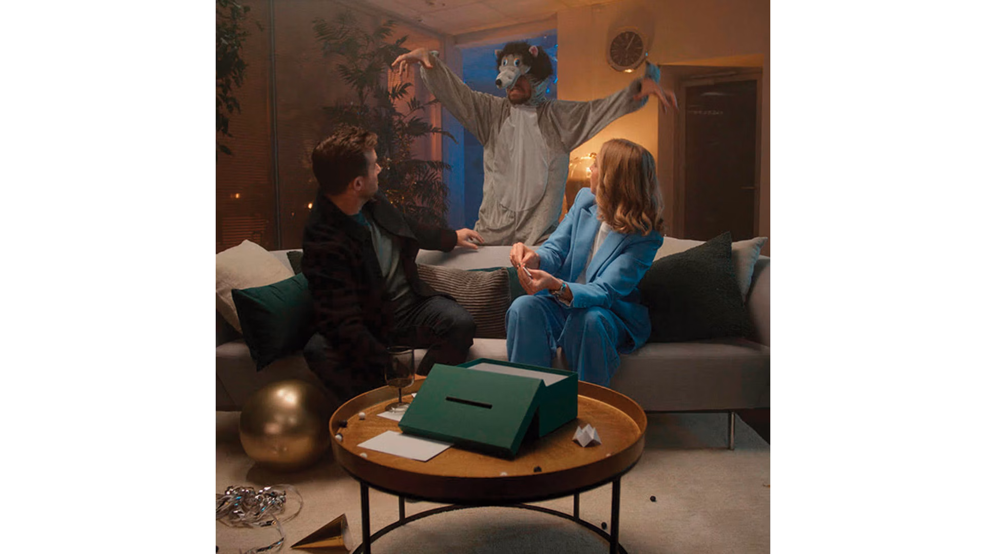 Image 57: Two people on a couch, startled by a person dressed as a wolf entering the room. 