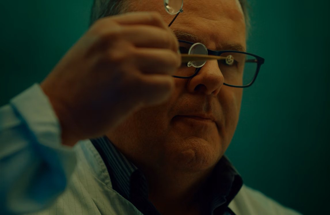 Relojero observando un componente de reloj minúsculo.